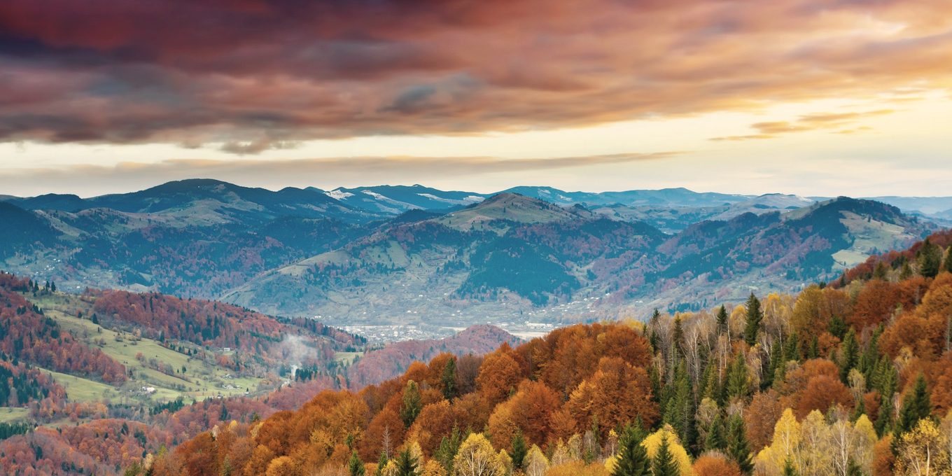 A wide valley of autumn forest below distant ridges