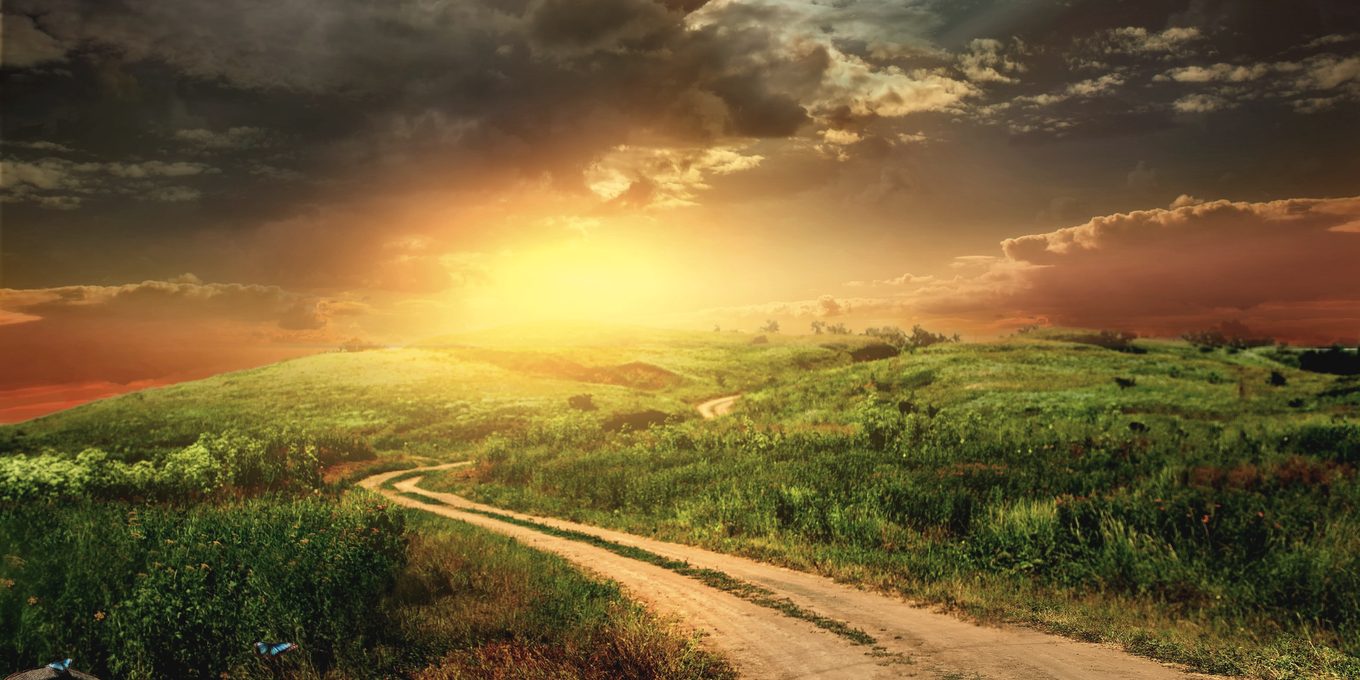 A dirt track climbing over a hill at sunset