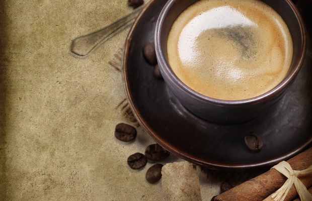 A cup of black coffee with cinnamon sticks on worn paper