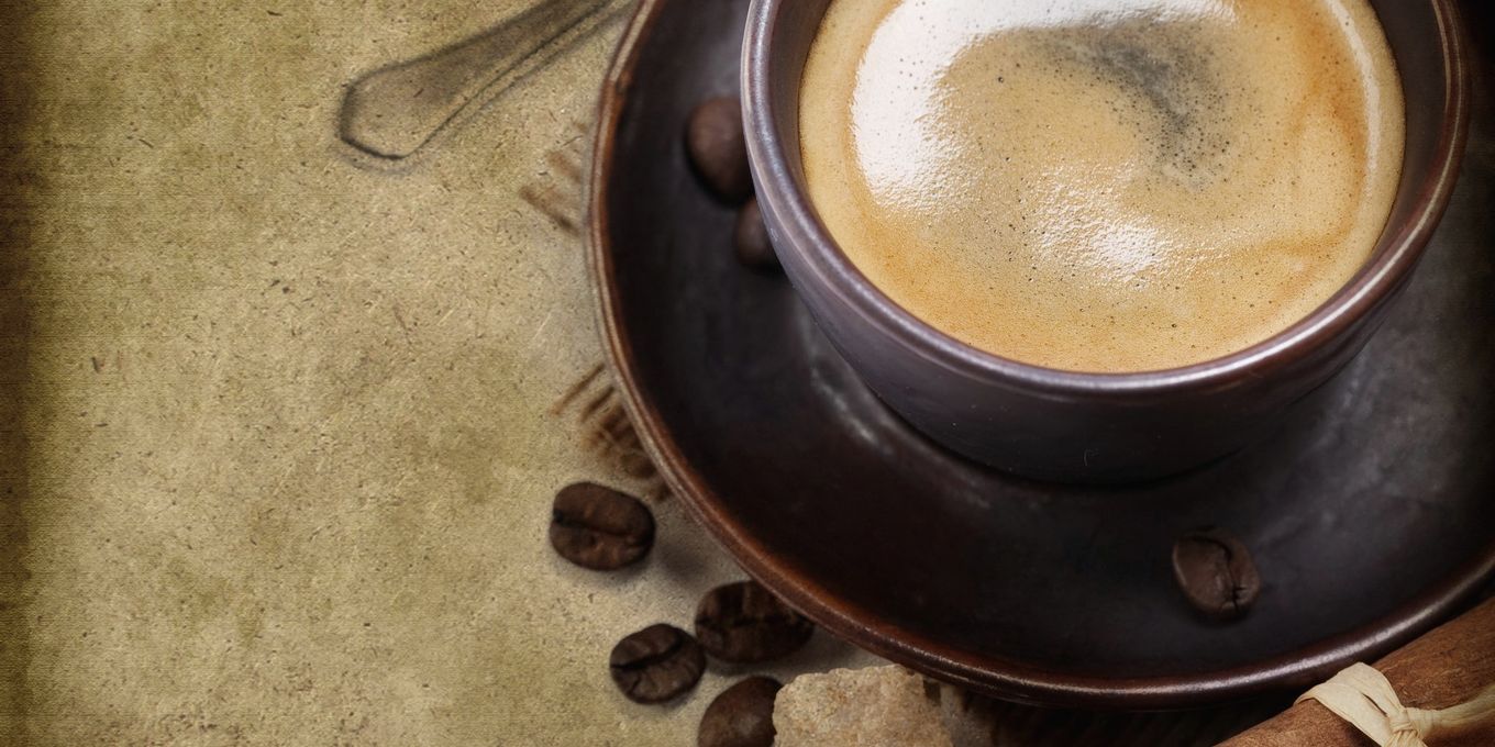 A cup of black coffee with cinnamon sticks on worn paper