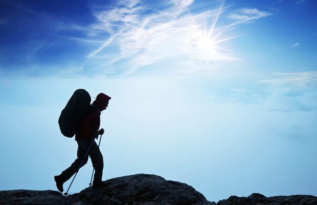 A hiker with trekking poles on a rocky crest against a bright sky
