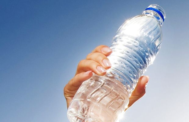 A hand holding a bottle of water up against a blue sky