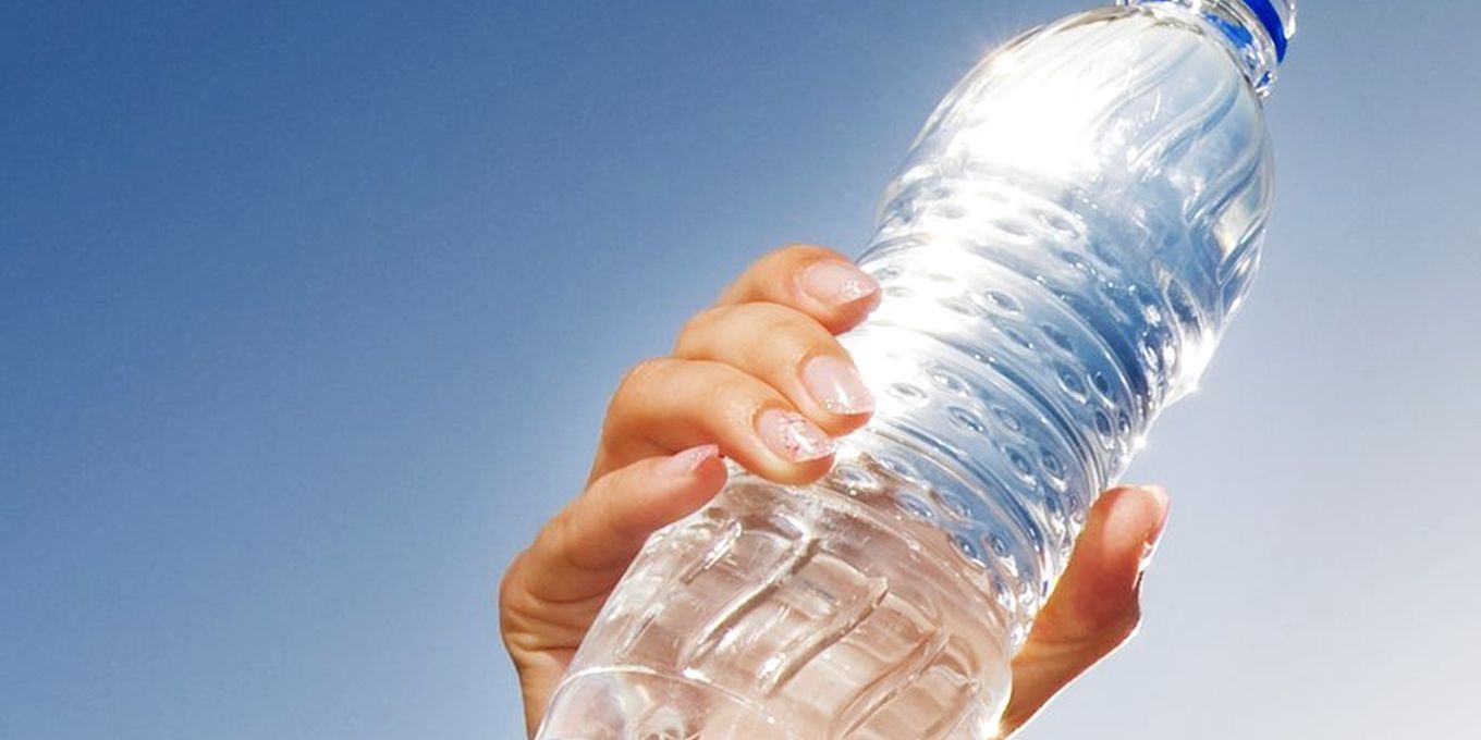 A hand holding a bottle of water up against a blue sky