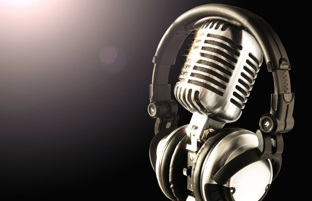 A chrome studio microphone with headphones hung over it